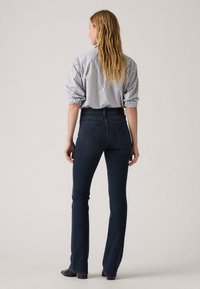 Women’s high-waisted denim flared jeans in dark blue, featuring five pockets, subtle stitching, and a smooth texture, paired with a striped shirt.