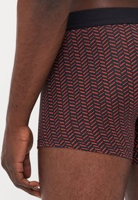 Herrens boxershorts i marinblått med ett rött fiskbensmönster. Har en svart elastisk midjeband och en slät, tight design.