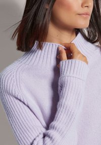 Helles lavendelfarbenes Strickpullover mit hohem Rippkragen und langen Ärmeln, der ein strukturiertes Muster auf dem Stoff aufweist.
