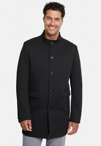 Abrigo negro con un alto cuello, enfrente de cinco botones y dos bolsillos laterales. Hecho de un tejido texturizado con una forma estructurada.