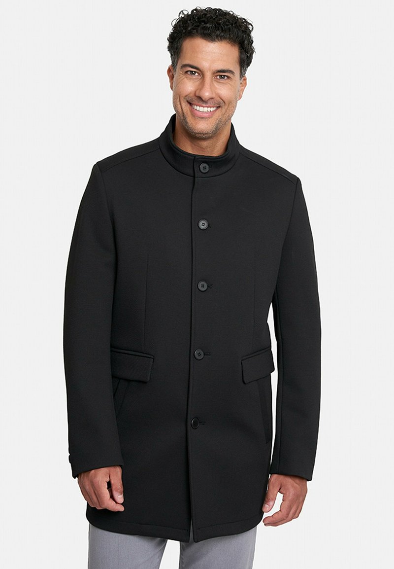 Abrigo negro con un alto cuello, enfrente de cinco botones y dos bolsillos laterales. Hecho de un tejido texturizado con una forma estructurada.