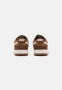 Smeđe suede tenisice s bijelim gumenim srednjim slojem, s zelenim dijelom na peti i bijelim Nike logom straga. Zaobljeni, podstavljeni ovratnik.