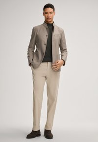 Graue Jacke aus Wollmischung mit Knopfverschluss, aufgesetzten Taschen, kombiniert mit einem dunklen Rollkragenpullover und hellfarbigen Hosen, abgerundet mit braunen Stiefeln.