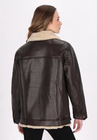 Giacca in pelle marrone con colletto in pelliccia, caratterizzata da una vestibilità ampia e cuciture visibili, mostrata da dietro. Superficie texture.