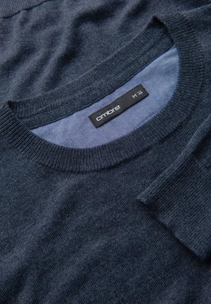 Maglione lavorato a maglia blu navy con collo rotondo, morbida consistenza e polsini a coste. Etichetta visibile con il nome del brand "ombré" e taglia "M".