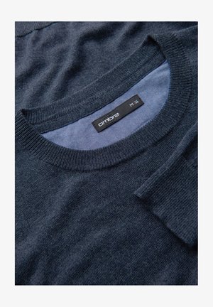 Maglione lavorato a maglia blu navy con collo rotondo, morbida consistenza e polsini a coste. Etichetta visibile con il nome del brand "ombré" e taglia "M".