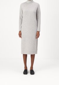Robe en maille côtelée gris clair avec un col montant, des manches longues et une longueur mi-mollet, associée à des mocassins noirs. Design simple et épuré.