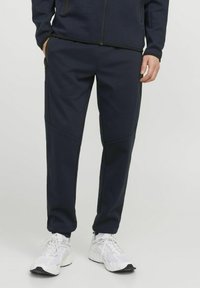 Pantalons de jogging bleu marine en tissu doux, dotés de poches latérales et de détails en panneau contrasté, associés à des chaussures de sport blanches.