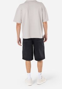 Vaalea harmaa teksturoitu lyhythihainen paita, yhdistetty mustiin farkkushortsihin. Jalkineina valkoiset lenkkarit, joita korostavat valkoiset sukat.