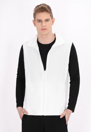 Witte fleece vest met rits en kraag, gemaakt van zacht materiaal, gedragen over een zwart langshirt; minimalistisch ontwerp en naadloze zijkanten.