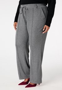 Grijze pantalon met krijtstrepen, gemaakt van zachte stof met een losse pasvorm, voorzien van zijzakken en een trekkoord in de taille. Gecombineerd met bordeauxrode hakken.