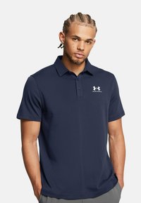 Marineblaues Polohemd aus glattem Stoff; verfügt über einen klassischen Kragen, kurze Ärmel und ein weißes Logo auf der linken Brust.