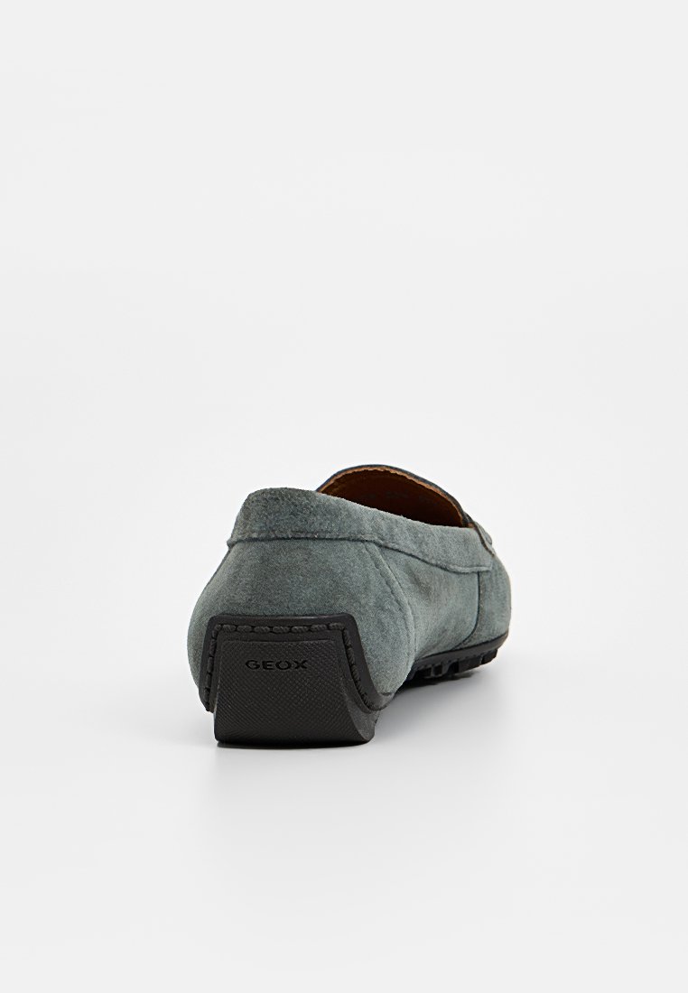 Bottine grise en daim à enfiler avec un dos arrondi, dotée d'une semelle en caoutchouc noir et de détails de couture subtils. Logo de la marque visible à l'arrière.