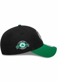 Cappello nero con visiera verde, con simboli celtici ricamati e una toppa che indica 'Celtics Champions'. Tessuto morbido con design strutturato.