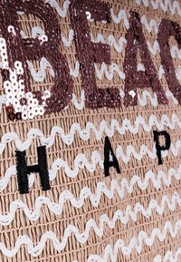 Geflochtene Strohtasche mit dem Wort "BEACH" aus Pailletten und "HAP" in schwarzem Stickerei, mit abwechselnden weißen und pinkfarbenen strukturierten Stichen.