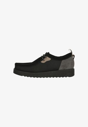 Black mesh and suede slip-on shoe with grey accents, round toe, textured midsole, and lacing detail, featuring a pull tab at the heel.