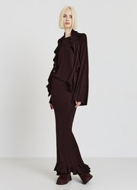 Langes braunes Kleid mit gerafften Akzenten an Ärmeln und Saum. Weicher, dehnbarer Stoff, figurbetonte Silhouette, kombiniert mit klobigen braunen Stiefeln.