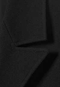 Close-up of a black wool coat collar with visible stitching and textured fabric.