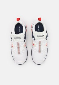 White sneakers with navy and red accents, mesh and synthetic material, thick soles, elastic laces, and a logo on the tongue.