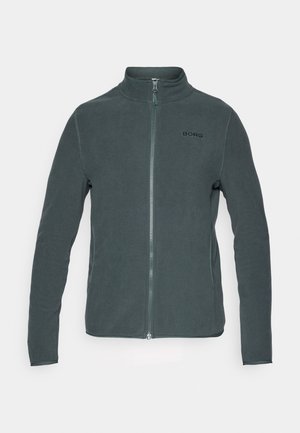 Pelēks vilnas džemperis ar augstu apkakli, pilnu rāvējslēdzēju un melnu logotipu kreisajā krūtī. Garas piedurknes ar gludu tekstūru.