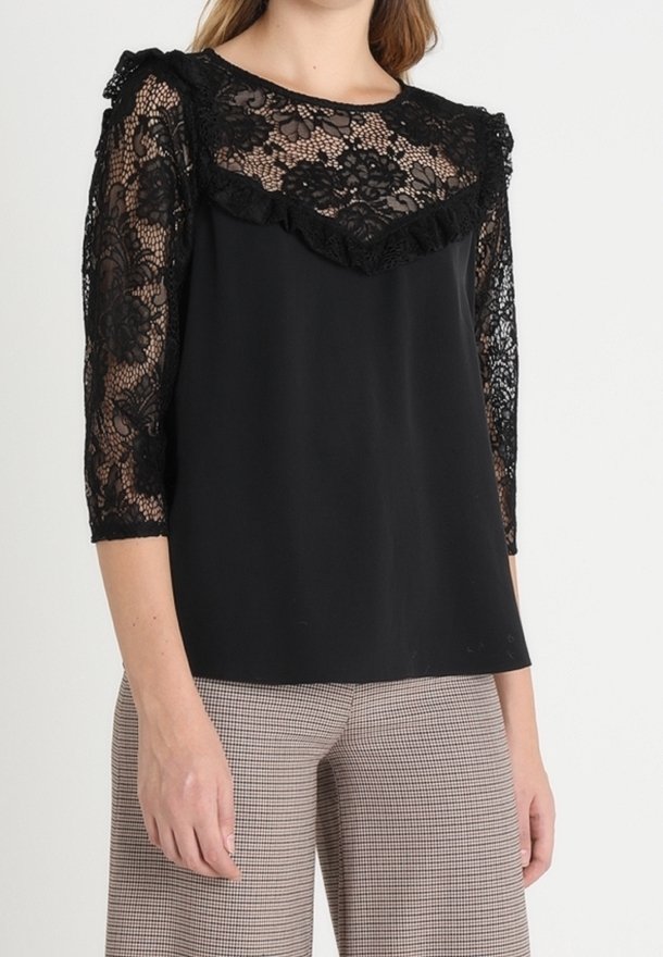 Blouse noire avec des manches en dentelle trois-quarts, un col froncé et un corps lisse. Portée sur un pantalon à carreaux à motifs.
