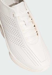 Baskets de sport blanches avec une tige en cuir perforée, design à lacets, bout rond et semelle texturée. Présente des détails de marque minimalistes.