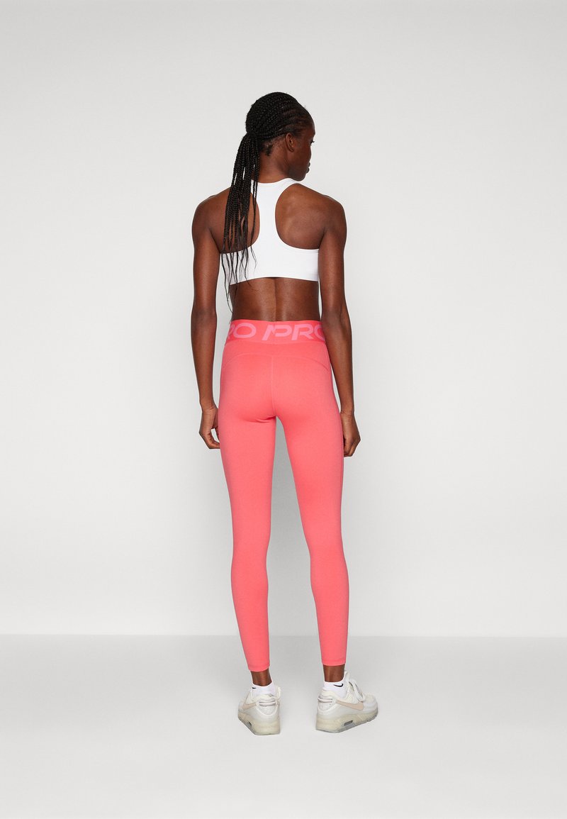 Leggings rosas con una cinturilla ancha que presenta un logo "PRO", combinados con una blusa blanca sin mangas. Tela suave y diseño ajustado.