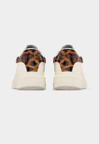 Ζευγάρι λευκά αθλητικά παπούτσια με παχιές σόλες και λεπτομέρειες με λεοπάρ σχέδιο στο πίσω μέρος, εμφανιζόμενα από πίσω με φόντο απλό.