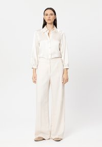 Satin cream blouse with button front and long puff sleeves, paired with high-waisted wide-leg trousers in matching color and texture.