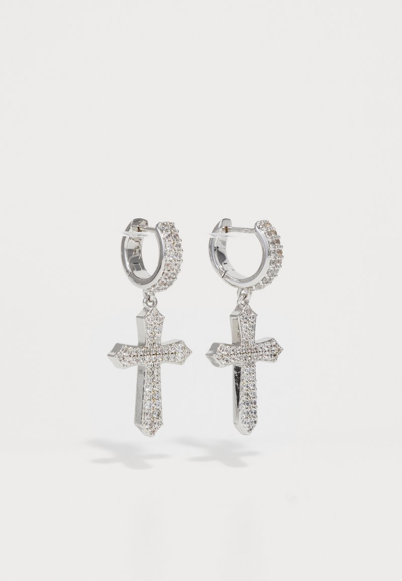 Boucles d'oreilles en argent en forme de créole avec des pendentifs en croix incrustés de petits cristaux transparents sur un fond blanc.
