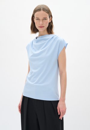 Haut bleu clair à manches courtes avec un col drapé, fabriqué en tissu doux. Associé à un pantalon noir taille haute pour un contraste.
