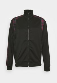 Giacca nera con zip e colletto alto. Presenta dettagli a motivi scozzesi in rosso e blu sulle spalle. Tessuto liscio, polsini e orlo elasticizzati.