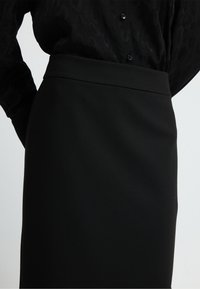 Schwarzer Bleistiftrock aus glattem Stoff, mit hohem Taillenbund und figurbetonter Silhouette, ohne sichtbare Muster oder Akzente.