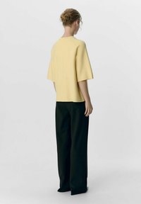 Un haut jaune à manches courtes associé à un pantalon large taille haute noir. Tissu lisse avec une coupe décontractée, montré de dos.