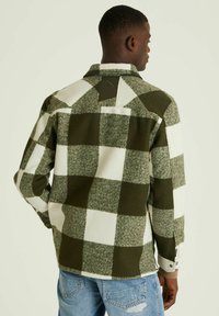 Groene en witte geruite fleecejack met een kraag, knopenmanchetten en een labeldetail op de rug. Zachte textuur en gestructureerde pasvorm.