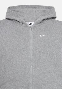 Sudadera con cremallera gris hecha de material de felpa suave, con capucha ajustable y un pequeño logo blanco de Nike en el área del pecho izquierdo.