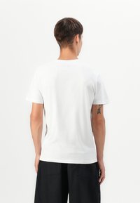 Hvid bomulds T-shirt med korte ærmer og rund hals, der har en glat tekstur. Bagsiden viser en subtil sømdetalje og et minimalt design.