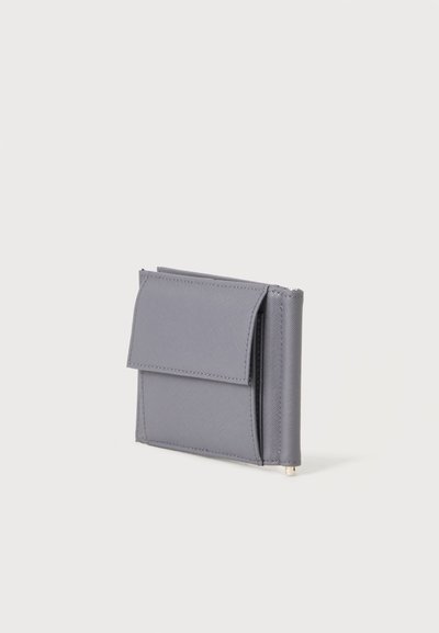 Portefeuille compact en cuir gris avec une poche à rabat avant et des bords cousus, debout sur un fond clair uni.