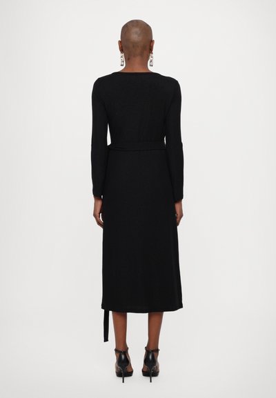 Vestido largo negro con mangas largas, cintura ceñida y corte recto que llega por debajo de las rodillas. Textura suave y diseño minimalista.