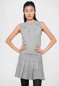 Top grigio senza maniche in maglia con applicazioni floreali, abbinato a una gonna grigia plissettata. L'outfit presenta un collo a coste e un contrasto di texture.