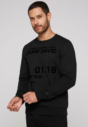 Sort sweatshirt med lange ærmer, der har fed grafisk tekst i forskellige nuancer af sort. Rund halsudskæring og ribbet manchetter.