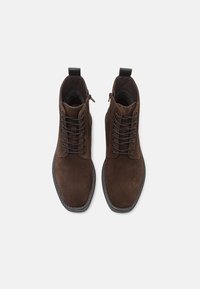 Brown suede ankle boots with a smooth texture, lace-up front, and side zipper, featuring a black rubber sole and stitched accents.