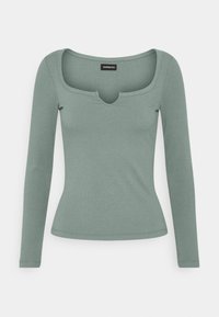 Langærmet, ribbet top i dæmpet grøn. Har en firkantet halsudskæring med en lav centerudskæring. Blød tekstur og tætsiddende design.