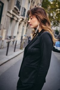 Noor naine musta naelutatud bleiseri ja pikkade hõbedaste kõrvarõngastega kõnnib linnatänaval, taustal on hooned ja autod.