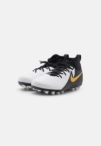 Scarpini da calcio Nike in bianco con accenti neri e dorati, caratterizzati da un design testurizzato, chiusura con lacci e una suola resistente con tacchetti.