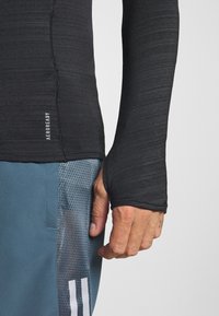 Czarna, długosleeve'owa koszulka sportowa wykonana z teksturowanego materiału, z otworem na kciuk, zestawiona z niebieskimi szortami z siateczkowymi panelami.