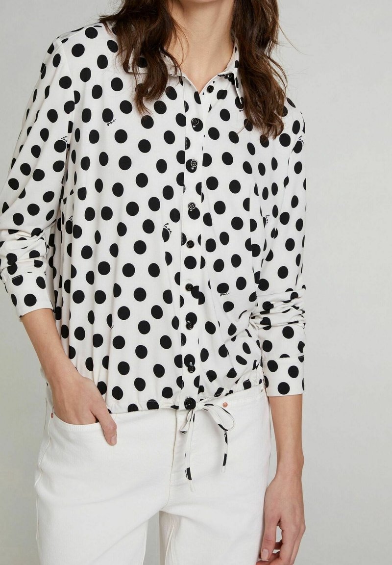 Camicia a maniche lunghe a righe bianche e nere con bottoni, caratterizzata da un vita con cordino e bottoni neri a contrasto su un tessuto liscio.