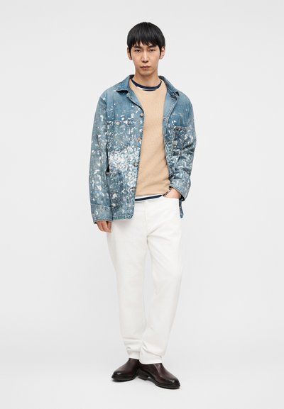 Τζιν μπουφάν με σχέδιο πιτσιλιών από μπογιά, μπεζ πουλόβερ από κάτω, λευκό παντελόνι και καφέ μποτάκια. Γενικά casual εμφάνιση σε ανοιχτά χρώματα.