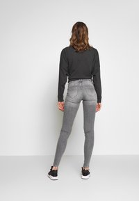 Jeans skinny de tiro alto grises y una camiseta de manga larga oscura, combinados con zapatillas negras. El conjunto presenta una silueta ajustada y un mínimo de detalles.