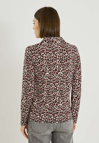 Blusa de manga larga en tela ligera con un diseño atrevido de estampado de leopardo en rojo y negro, con cuello y silueta ajustada.